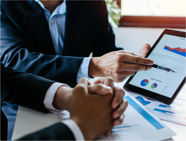 Two men wearing suits and looking at some charts in a tablet.